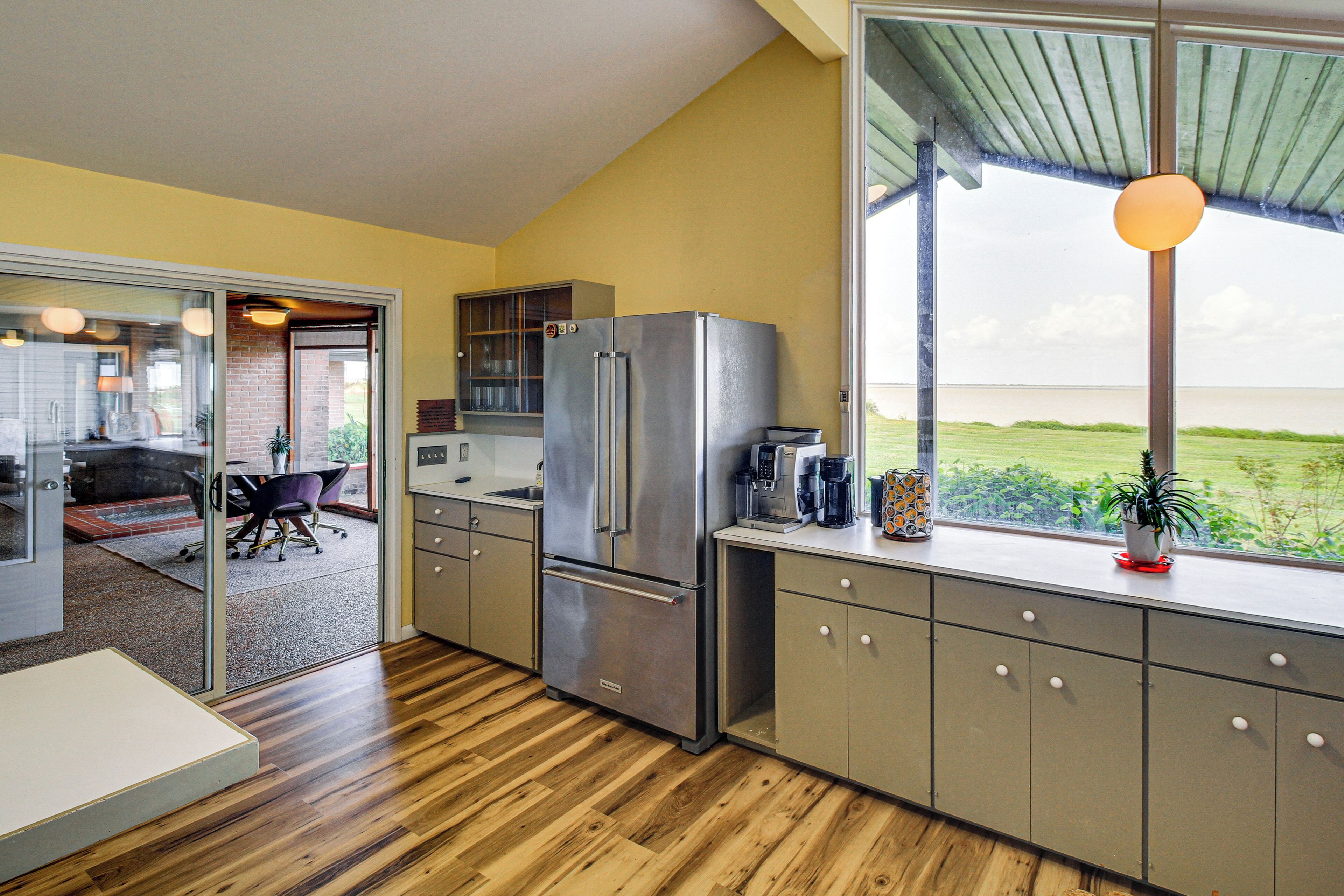 A modern kitchen with a stainless steel refrigerator, wooden flooring, and a view of the outdoors.
