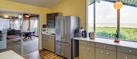 A modern kitchen with a stainless steel refrigerator, wooden flooring, and a view of the outdoors.