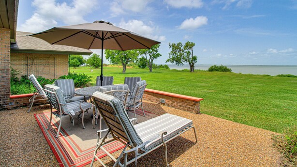 An outdoor patio with a table and chairs, a large umbrella, and a view of a lake. - Bayfront Escape Near Boat Launch in Austwell (Austwell)