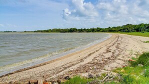 A beach with a sandy shore, a calm sea, and a line of trees in the background. - Bayfront Escape Near Boat Launch in Austwell (Austwell)