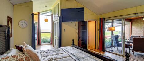 Un dormitorio con cama, ventilador de techo, ventana con cortinas y vistas al exterior.