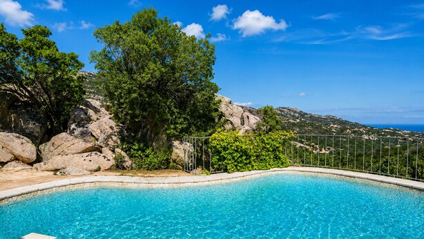 A clear blue pool surrounded by natural rock formations and trees, with a view of the sea in the background. - Porto Cervo - Villa AUREA Retreat (Arzachena)