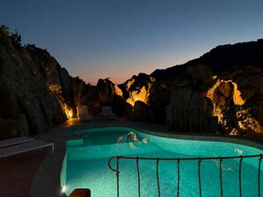 Ein Schwimmbecken mit Blick auf felsige Klippen im Abendlicht.