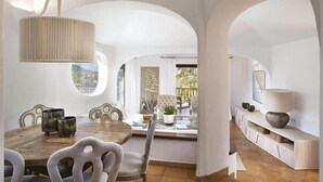 A dining area with a wooden table and chairs, a hanging light fixture, and a view through an arched window. - Porto Cervo - Villa AUREA Retreat (Arzachena)