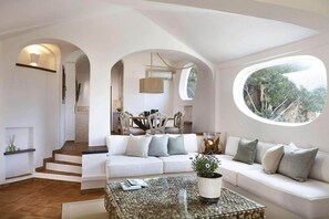 Ein modernes Wohnzimmer mit einem weißen Sofa, einem Couchtisch mit Pflanze und Blick durch ein großes Fenster.