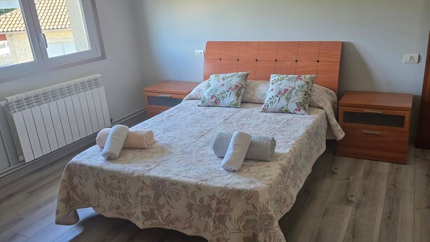 Een slaapkamer met een bed, twee nachtkastjes, een houten deur en een raam.