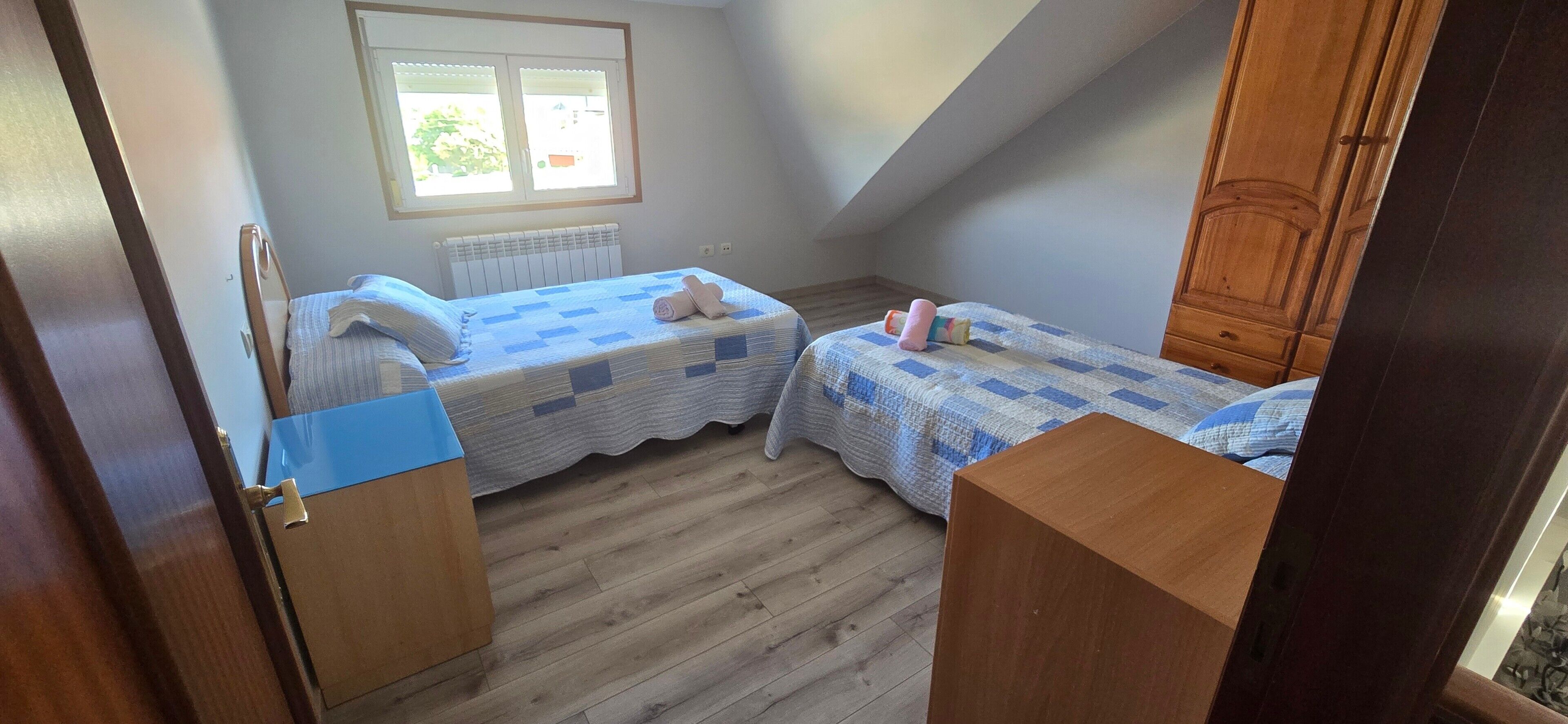 Een kleine kamer met twee bedden, een radiator, een raam en houten vloeren.