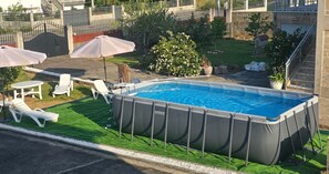 An outdoor swimming pool with a surrounding deck, lounge chairs, and a covered patio area.