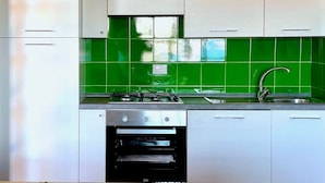 A kitchen with white cabinets, a green tiled backsplash, a sink, a stove, and an oven. - Punta Est - PERLA Two-Bedroom Apartment with Terrace and Ocean View (Capo Coda Cavallo)