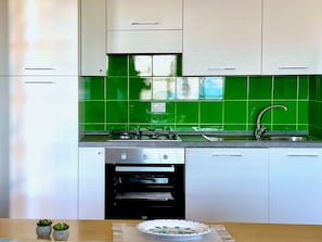 Eine Küche mit weißen Schränken, einer grünen Fliesenrückwand, einem Spülbecken, einem Herd und einem Backofen.