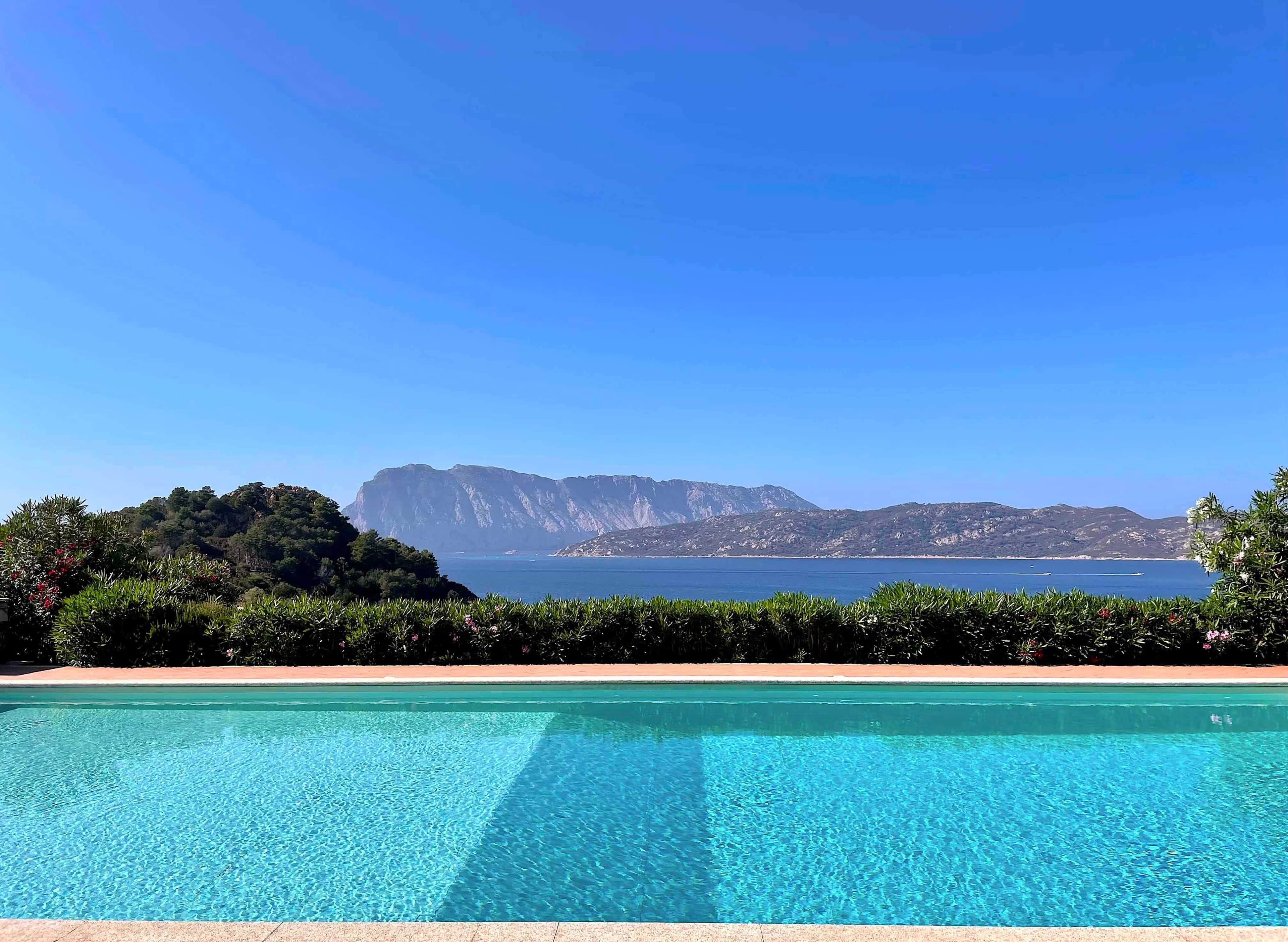 A clear blue pool with a view of a mountainous landscape and the sea.