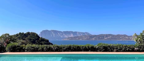Una piscina azul cristalina con vistas a un paisaje montañoso y al mar.