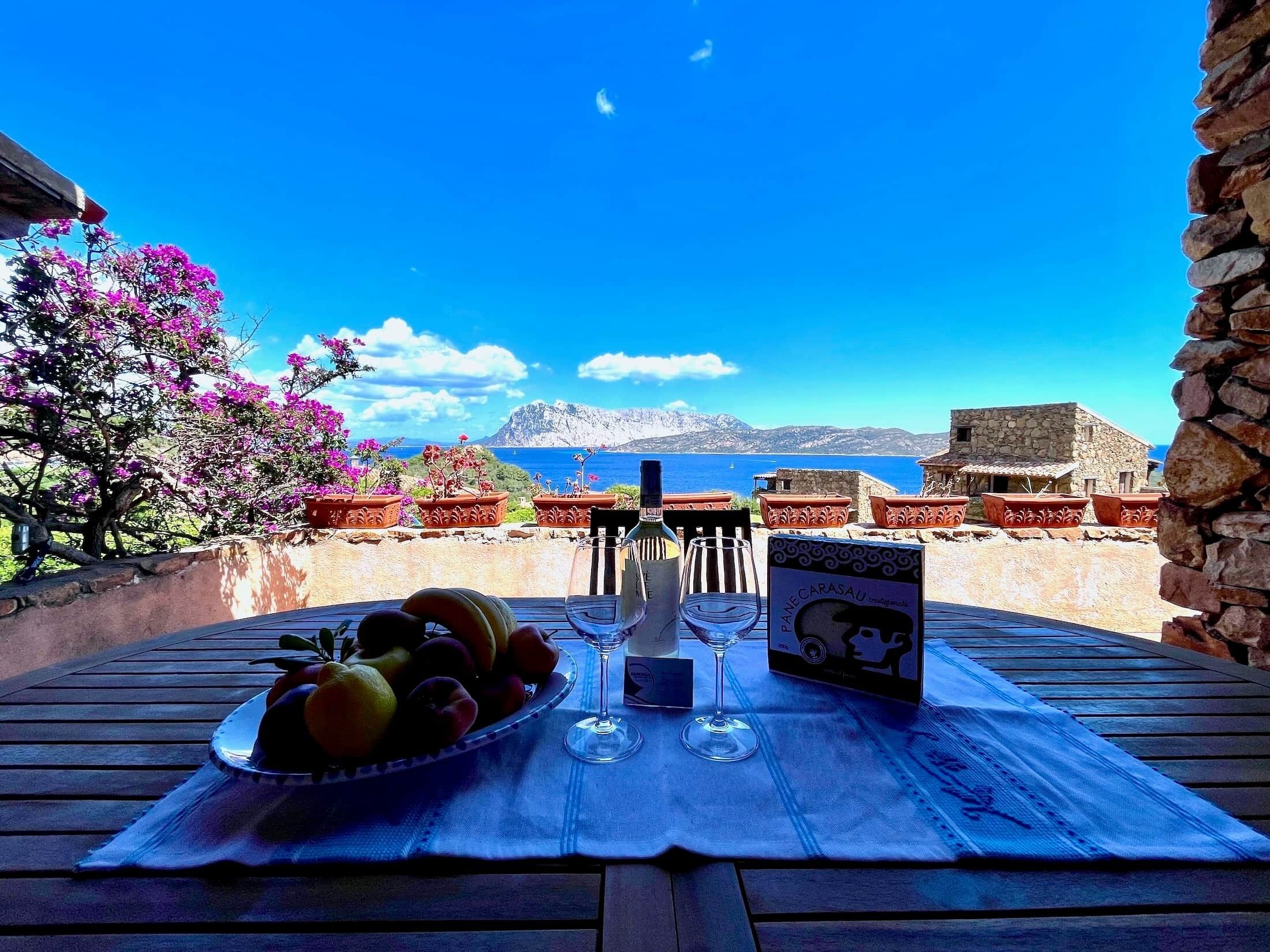 Een tafel met een fles, glazen en een wijnbox op een terras met uitzicht op een prachtig landschap.