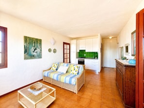 A living room with a sofa, a glass coffee table, and a painting on the wall. - Punta Est - PERLA Two-Bedroom Apartment with Terrace and Ocean View (Capo Coda Cavallo)
