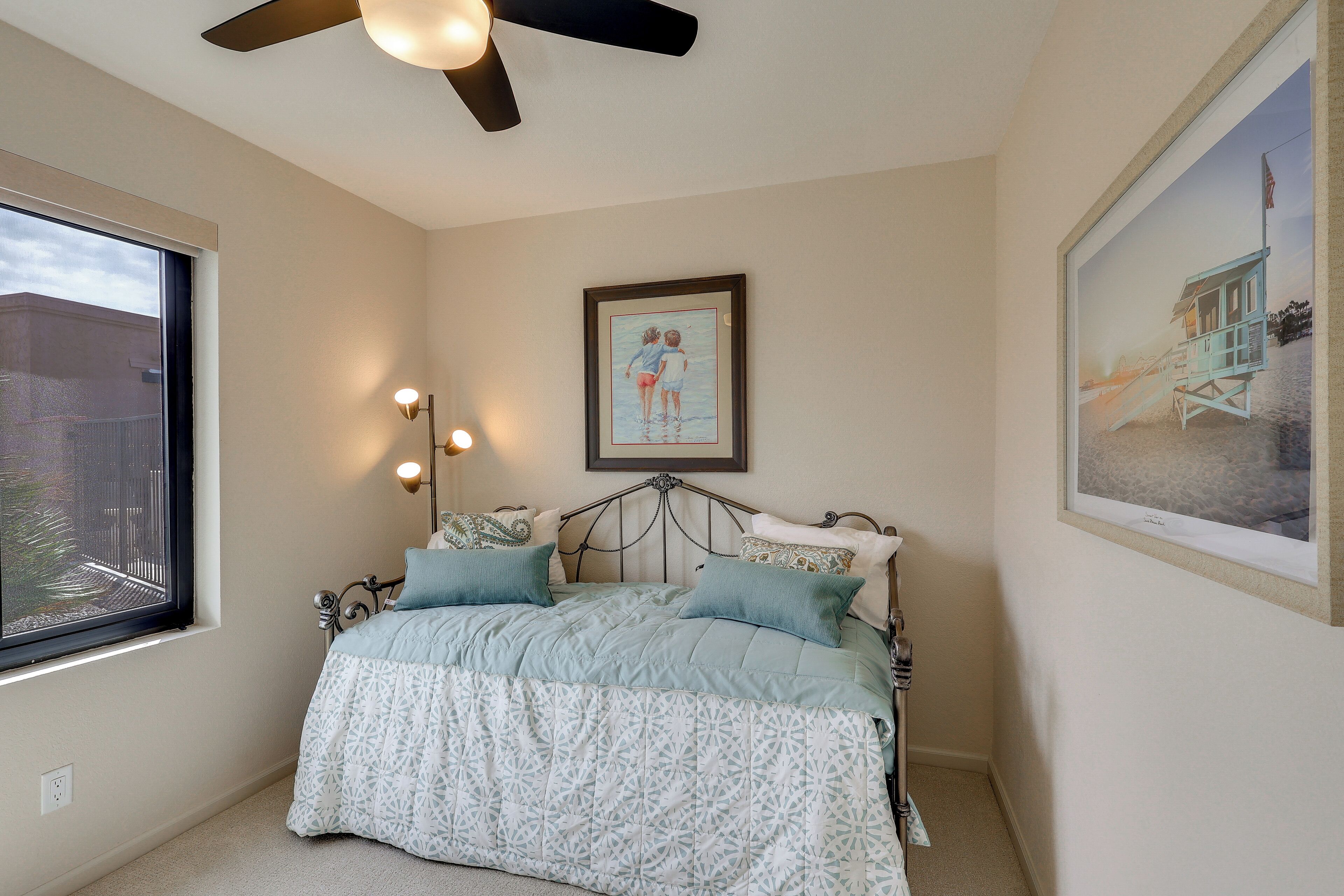 A bedroom with a bed, a ceiling fan, a window, and a painting on the wall.