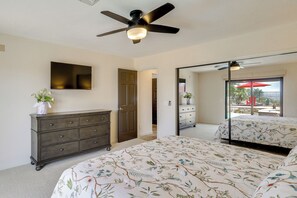 Ein Schlafzimmer mit Bett, Schminktisch, Deckenventilator und einem großen Spiegel, der einen Balkon mit Gartenmöbeln reflektiert.