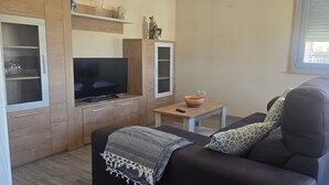 Ein kompakter Wohnbereich mit einer Couch, einem Fernseher, einem kleinen Tisch und einer Vitrine.