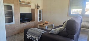 Un espace de vie compact comprenant un canapé, un téléviseur, une petite table et un meuble avec des portes en verre.