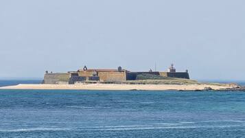 A coastal fortification with a lighthouse, situated on a sandy beach with the sea in the foreground.