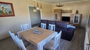 Ein Essbereich mit Holztisch und weißen Stühlen, einem braunen Sofa und einem Fernseher.
