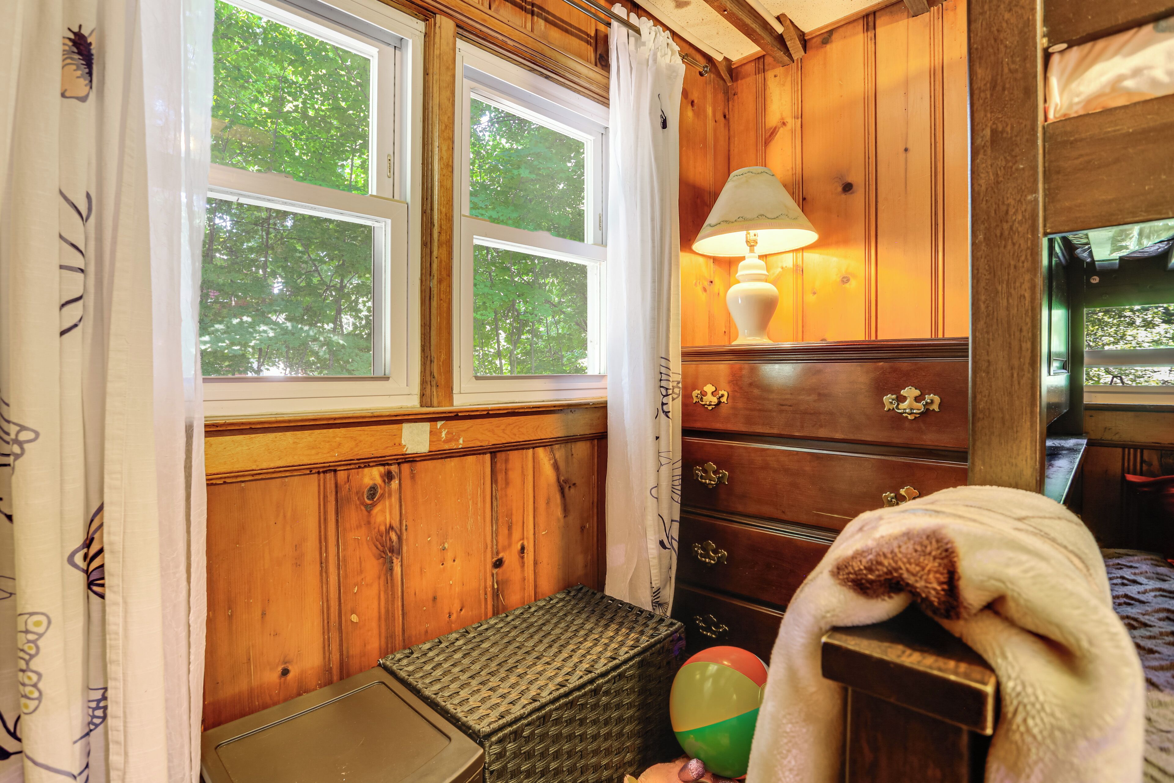 A wooden room with two windows, a lamp, a dresser, and a pet dog.