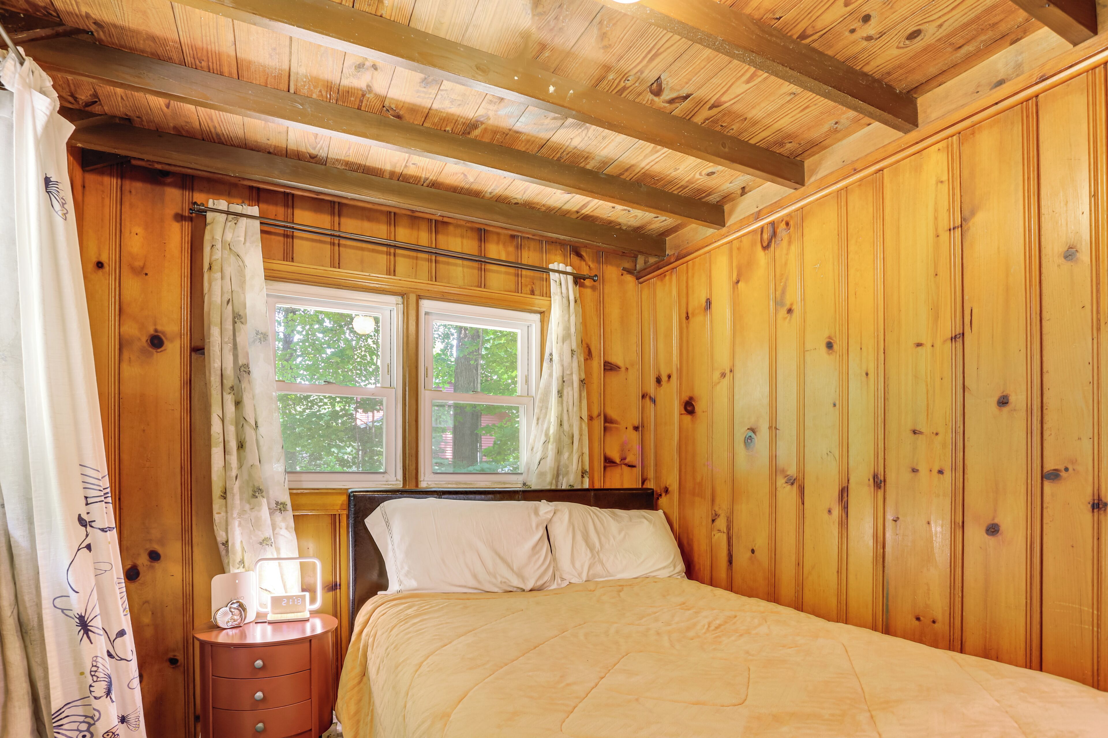 A wooden-paneled room with a bed, a nightstand, and a window with curtains.
