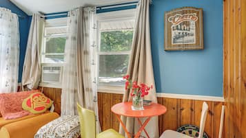 A room with a window, a dartboard, a table with a vase of flowers, and a chair.