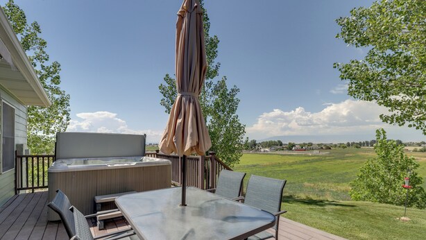 Eine Terrasse im Freien mit einem Glastisch, Metallstühlen, einer gepolsterten Bank und einem großen Sonnenschirm.