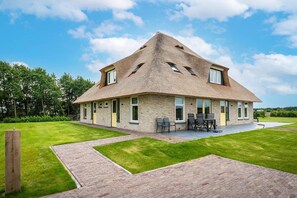 A house with a sloped roof, a brick exterior, and a paved patio with outdoor furniture. - Farmhouse near De Koog (De Koog)