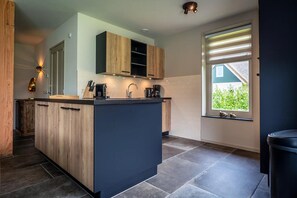 A modern kitchen with a central island, wooden cabinets, a built-in oven, and a window with blinds. - Farmhouse near De Koog (De Koog)