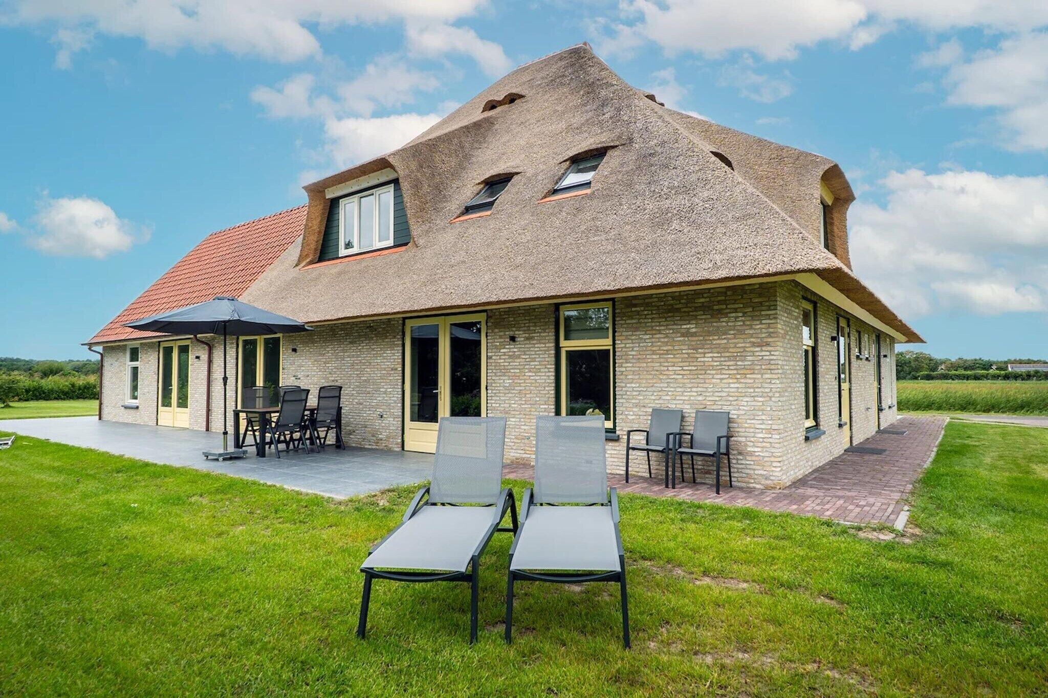 A house with a sloped roof, a patio with chairs, and a grassy lawn.
