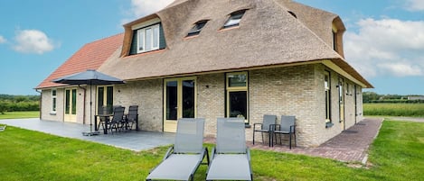 Una casa con techo inclinado, un patio con sillas y un césped.