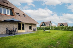 A residential property with a brick exterior, a thatched roof, a lawn, and a patio area with outdoor furniture. - Farmhouse near De Koog (De Koog)