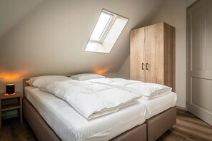 A bedroom with a sloped ceiling, a skylight, a bed with white bedding, a wooden wardrobe, and a bedside lamp. - Farmhouse near De Koog (De Koog)