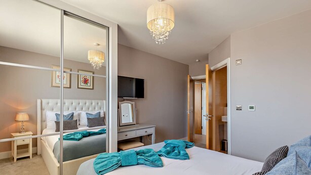 Ein modernes Hotelzimmer mit einem großen Bett, einem Nachttisch, einem Schreibtisch, einem Fernseher und einem Spiegel.