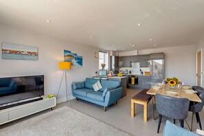 A modern living space with a sofa, TV, dining table, and kitchen area.