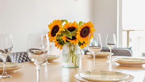 Ein Esstisch gedeckt mit Tellern, Gläsern und einer Vase mit Sonnenblumen.