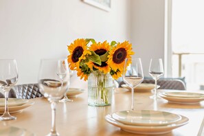 A dining table set with plates, glasses, and a vase with sunflowers. - Ocean View Beach Apartment with Balcony & Parking (Bournemouth, Christchurch and Poole)