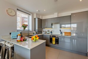 A modern kitchen with a central island, stainless steel appliances, and a window with blinds. - Ocean View Beach Apartment with Balcony & Parking (Bournemouth, Christchurch and Poole)
