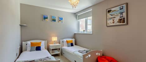 A bedroom with two beds, a nightstand, a red bean bag, a chandelier, and wall art.