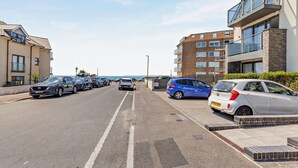 Eine Wohnstraße mit geparkten Autos, blauem Himmel und mehrstöckigen Gebäuden mit Balkonen.