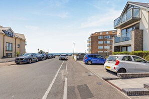 A residential street with parked cars, a clear sky, and multi-story buildings with balconies. - Ocean View Beach Apartment with Balcony & Parking (Bournemouth, Christchurch and Poole)