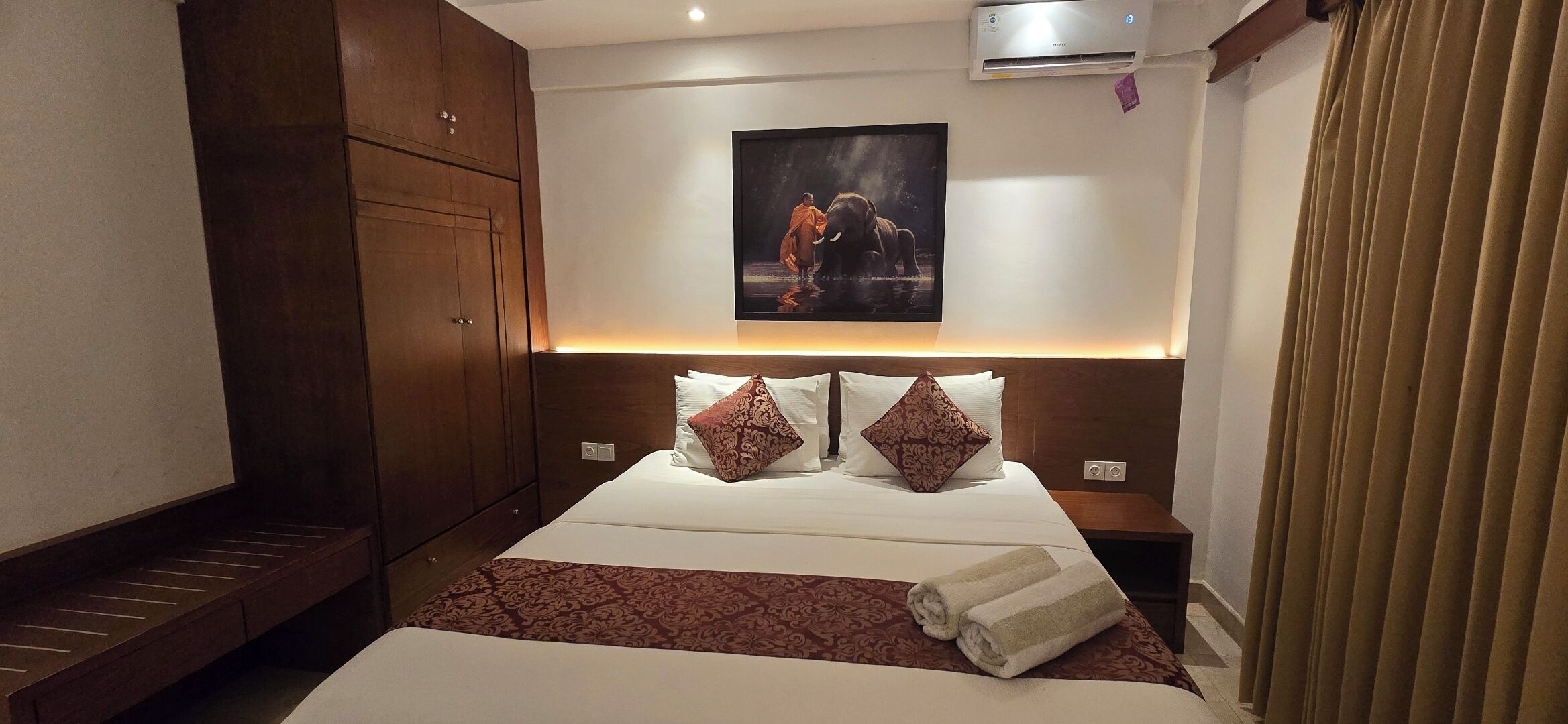 A hotel room with a bed, a headboard with a picture, a wardrobe, and a nightstand.