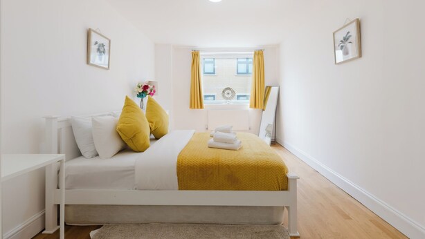 Une chambre à coucher avec un lit, une table de chevet, une fenêtre avec des rideaux et un tableau accroché au mur.