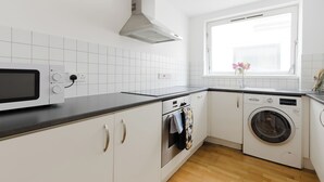 Une cuisine moderne avec des meubles blancs, un four à micro-ondes, un four traditionnel et un lave-linge.