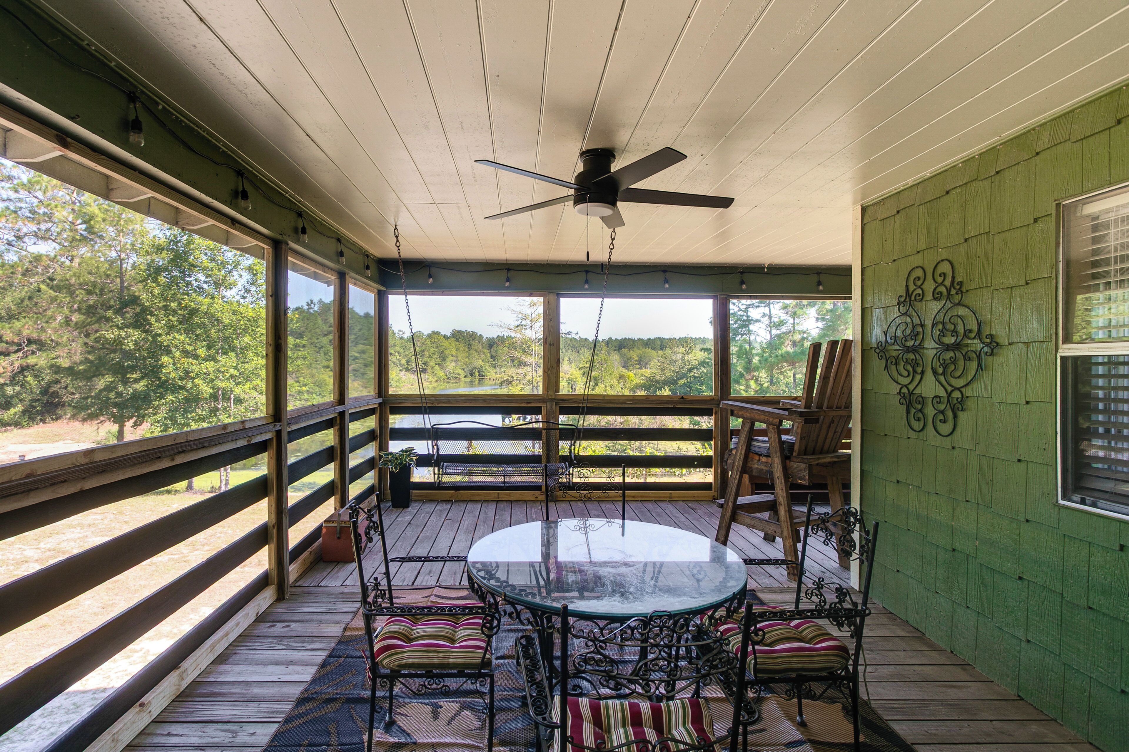 A covered outdoor patio with a round table and chairs, a ceiling fan, and a view of a natural landscape.