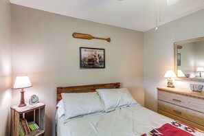 Un dormitorio con una cama de madera, una mesita de noche con lámpara, un cuadro en la pared y un aparador con espejo.
