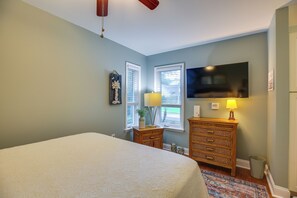A bedroom with a bed, dresser, TV, windows, and a lamp. - 1 BR Ocean Inlet View with Private Pool (Murrells Inlet)