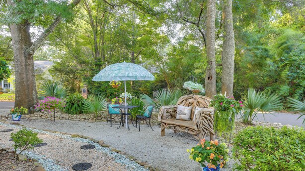 A garden patio with a table and chairs, a wicker bench, and a decorative umbrella. - 1 BR Ocean Inlet View with Private Pool (Murrells Inlet)