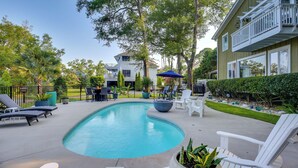 A swimming pool with lounge chairs and umbrellas, surrounded by a fence and greenery. - 1 BR Ocean Inlet View with Private Pool (Murrells Inlet)